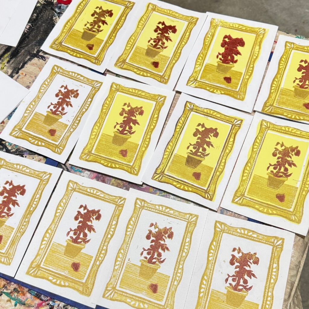 A grid of small mixed-media prints shows potted plants framed in gold with repeated hand-printed textures and warm yellow backgrounds.
