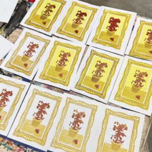A grid of small mixed-media prints shows potted plants framed in gold with repeated hand-printed textures and warm yellow backgrounds.