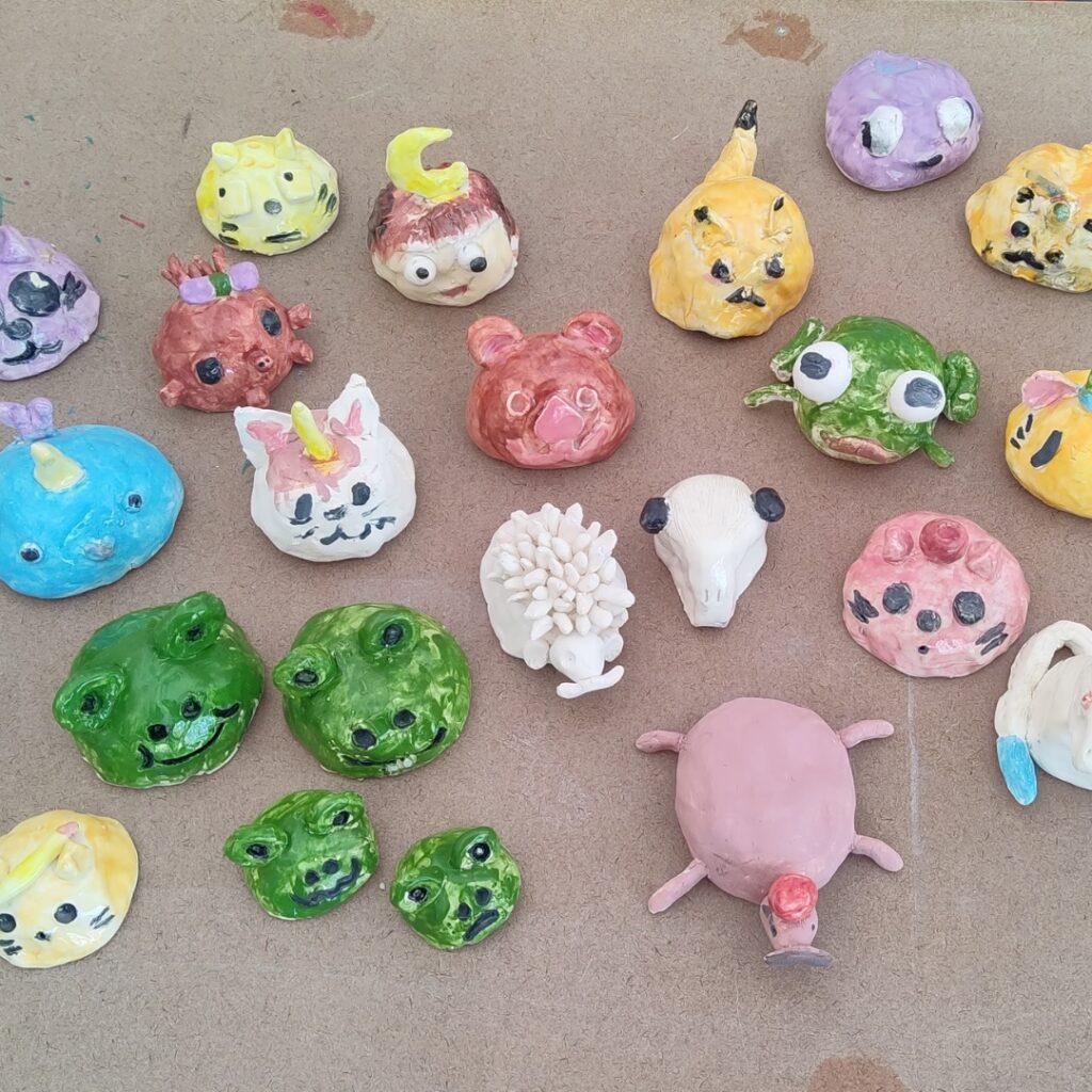 Hand-painted clay animal and character sculptures created by youth artists, arranged on a tabletop.